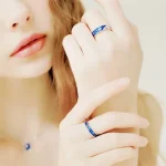 Damenhände mit silbernem Ring und Halskette, verziert mit blauen Steinen, stilvoll präsentiert. Perfekt für Schmuckliebhaber und elegante Outfits.