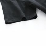 Nahaufnahme eines schwarzen Baumwoll-T-Shirts mit weicher Textur, liegend auf weißem Hintergrund, detailreiche Stoffstruktur sichtbar.