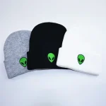 Drei Alien-Design-Mützen in Grau, Schwarz und Weiß mit grünem Alien-Logo, ideal für Science-Fiction-Fans und trendige Accessoires.