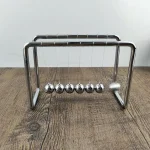 Metallisches Pendel-Experiment zur Demonstration der Schwerkraft, bestehend aus Kugeln an Schnüren, auf Holztisch.