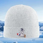 Weiße, gestrickte Mütze mit Weltraum-Motiv, einem kleinen Astronauten auf einer Rakete, vor einer winterlichen Berglandschaft. Perfekt für Kinder, die Science-Fiction und Weltraum lieben.