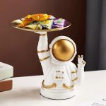 Niedliche Astronauten-Dekofigur mit goldenem Helm, die ein Tablett mit Süßigkeiten hält, ideal für Science-Fiction- und Weltraumthemen.