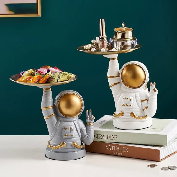 Zwei Astronauten-Dekorationsfiguren mit goldenen Helmen, die auf einer weißen Oberfläche stehen, halten silberne Tabletts mit Schmuck und Süßigkeiten, ideal für Science-Fiction-Dekor.