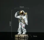 Detailaufnahme einer Raumfahrerfigur mit goldfarbenem Helm, weißem Raumanzug und Rucksack, Maße: 23 cm hoch, 13 cm breit, auf einem Holzsockel stehend.