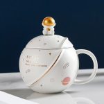 Weiße Teetasse mit Raumfahrt-Design, inklusive goldener Sternen- und Planetenmotive, ideal für Science-Fans und Dekoration.