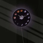 Moderne Wanduhr mit Mondphasen-Design, zeigt die verschiedenen Phasen des Mondes in einem stilvollen schwarzen Rahmen, ideal für Wissenschafts- und Dekorationsliebhaber.