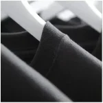 Schwarzes T-Shirt auf Kleiderbügel, Nahaufnahme, modisches Basic, weiches Material, elegante Kleidung, Alltagslook, stilvoller Casual-Look, Textil-Detailaufnahme, Modeaccessoire, Bekleidung, Fashion.