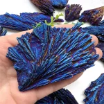 Nahaufnahme von leuchtend blauen Mineralien und Kristallen, die in einer Hand gehalten werden, mit weiteren Kristallen im Hintergrund.