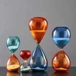Bunte Sanduhren in verschiedenen Größen und Farben, die auf einem schwarzen Tisch stehen, symbolisieren Zeit und Wissenschaft in moderner Dekoration.