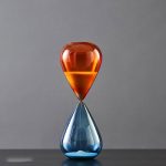 Elegante Glas-Sanduhr mit rotem oberen und blauen unteren Teil, ideal als wissenschaftliches Dekorationsstück oder Geschenk.