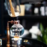 Siphon-Kaffeepot für wissenschaftliche Kaffeezubereitung, mit Glasbehälter und Kupferrohren, auf einer schwarzen Oberfläche.