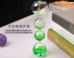 Glas-Sanduhr mit grüner Flüssigkeit, die zwischen den Kammern fließt, auf einem weißen Tisch neben Büchern.