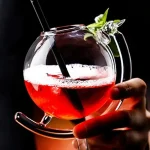 Ein schwarzer Cocktail in einem transparenten Glas mit Strohhalm und Minzblatt, perfekt für Cocktail-Liebhaber.