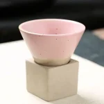 Elegante rosa Keramikschale auf einem quadratischen Betonquader, ideal für wissenschaftliche Dekorationen oder moderne Raumgestaltung.