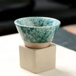 Handgefertigte Keramikschale mit blauer Glasur auf einem weißen Würfel-Stand, ideal für wissenschaftliche Dekorationen oder Sammlerstücke.