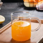 Transparentes Glas mit chemischer Strukturzeichnung, gefüllt mit orangefarbiger Flüssigkeit, auf Holztablett, wissenschaftliches Dekor, Nahaufnahme.