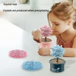 Mädchen beobachtet einen Kristallbaum, der durch Kristallisation entsteht, mit weiteren Kristallbaum-Dekorationen auf dem Tisch.