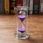 Elegante Sanduhr mit violettem Sand, ideal als wissenschaftliches Dekorationsstück oder Geschenk. Transparentes Glasgehäuse zeigt den fließenden Sand.