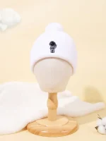 Weißer Kinder-Strickmütze mit Astronauten-Design, ideal für kalte Tage, auf einem Holzständer präsentiert.