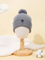 Graue Wollmütze mit Bommel auf einem Holzständer, ideal für kalte Tage, stilvoll und warm, perfekt für Wintermode.