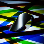 Hochwertige, moderne Computermaus mit reflektierender Oberfläche auf einem farbenfrohen, geometrischen Hintergrund. Perfekt für Technik- und Wissenschaftsdekorationen.