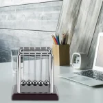 Klassische Newton-Wiege mit fünf Metallkugeln auf einem weißen Tisch, ideal für physikalische Experimente und wissenschaftliche Dekorationen.