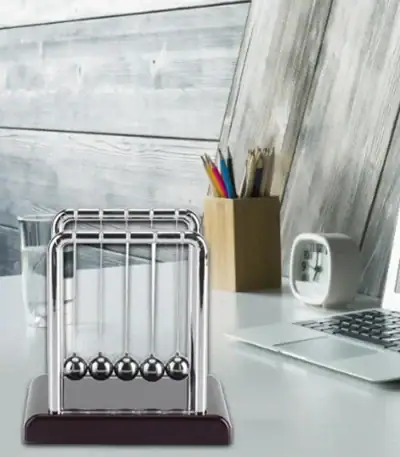 Klassische Newton-Wiege mit fünf Metallkugeln auf einem weißen Tisch, ideal für physikalische Experimente und wissenschaftliche Dekorationen.