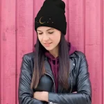 Schwarze Mütze mit Mond- und Sternmotiven, ideal für kalte Tage, kombiniert mit dunklem Haar und Lederjacke vor pinkem Holz.