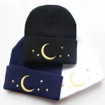Drei gestrickte Mützen in Schwarz, Blau und Weiß mit goldenen Mond- und Sternmotiven, ideal für kalte Tage, stilvoll und bequem.
