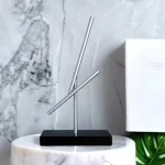 Modernes Metall-Himmelskörper-Dekorationsstück mit zwei schrägen Stäben auf schwarzem Sockel, ideal für wissenschaftliche oder dekorative Zwecke.