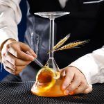 Nahaufnahme eines Wissenschaftsexperiments mit einem Reagenzglas, das eine orange Flüssigkeit enthält, während eine Person mit einer Pipette eine Probe entnimmt. Im Hintergrund sind weitere wissenscha.
