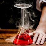 Wissenschaftliches Chemie-Experiment mit einem Reagenzglas, das eine rote Flüssigkeit enthält, auf einem Holztablett.