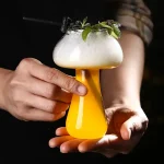 Kreatives Getränk in einem einzigartigen Glas, das wie ein wissenschaftliches Experiment aussieht, mit Kräutern und Blüten dekoriert.