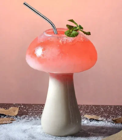Kreatives Blumenmushroom-Getränk mit rosa Flüssigkeit, Minzblatt und Strohhalm, auf einem dekorativen Untergrund mit Blättern und Salz.