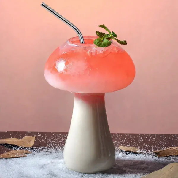 Kreatives Blumenmushroom-Getränk mit rosa Flüssigkeit, Minzblatt und Strohhalm, auf einem dekorativen Untergrund mit Blättern und Salz.