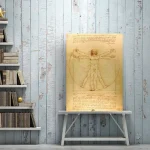 Detailliertes Poster des Vitruvianischen Menschen von Leonardo da Vinci, das die Proportionen des menschlichen Körpers zeigt, auf einem weißen Holzständer vor einer hellblauen, rustikalen Wand.