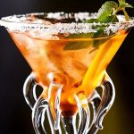 Ein farbenfroher Cocktail in einem einzigartigen Glas mit Salzrand, Minzblättern und Eiswürfeln, ideal für Partys und besondere Anlässe.