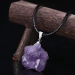 Lila Amethyst Kristallanhänger an schwarzem Lederband, auf Holzstange präsentiert, für Schmuck und Dekoration.