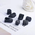 Sechs schwarze Gagat-Steine auf einer weißen Oberfläche, die wissenschaftliche Mineralienproben darstellen.