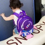 Kind mit Weltraum-Rucksack, der auf einer blauen Metallwand steht.