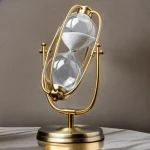 Elegante Sanduhr mit goldfarbenem Rahmen und klarer Glaskugel, die weißen Sand enthält, auf einem weißen Marmortisch.