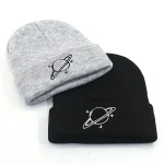 Zwei Beanies mit Planetensymbolen, eines grau mit Saturn und eines schwarz mit Saturn, ideal für Wissenschafts- und Astronomie-Fans.