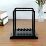 Klassischer Newtonpendel mit schwarzen Kugeln auf Holzoberfläche, ideal für wissenschaftliche Dekoration und physikalische Experimente.