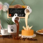 Zwei kreative Kaffeetassen-Dekorationen, die wie fließender Kaffee aussehen, auf einem Holztablett mit Kaffeebohnen, Blumentopf und einem kleinen Schiefertafel-Schild mit "Coffee Bar" Schriftzug.