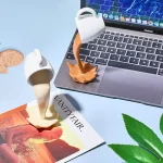 Kreatives Wissenschaftsdekor mit Miniatur-Öfen, die flüssige Substanzen in verschiedenen Farben darstellen, auf einem Laptop und Zeitschrift platziert. Perfekt für Wissenschafts- und Dekorationsliebha.