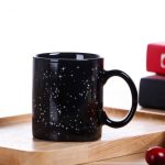 Schwarze Kaffeetasse mit weißen Sternen, ideal für Wissenschafts- und Dekorationsliebhaber, auf einem Holztablett präsentiert.