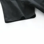 Nahaufnahme eines schwarzen Baumwoll-T-Shirts, das flach auf weißem Hintergrund liegt, zeigt die Textur und den Saum des Stoffes.
