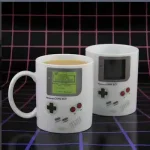 Tasse im Design eines klassischen Game Boy, perfekt für Gaming-Fans, mit Kaffee oder Tee gefüllt, auf einem schwarzen Gitterhintergrund.