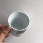 Weißer wissenschaftlicher Becher, gehalten von einer Hand, auf einem hellen Hintergrund. Perfekt für Wissenschafts- und Dekorationsliebhaber.