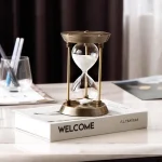 Eleganter Sanduhr-Timer aus Glas und Metall auf einem weißen Buch mit "WELCOME" Schriftzug, ideal für wissenschaftliche Dekorationen und moderne Inneneinrichtung.